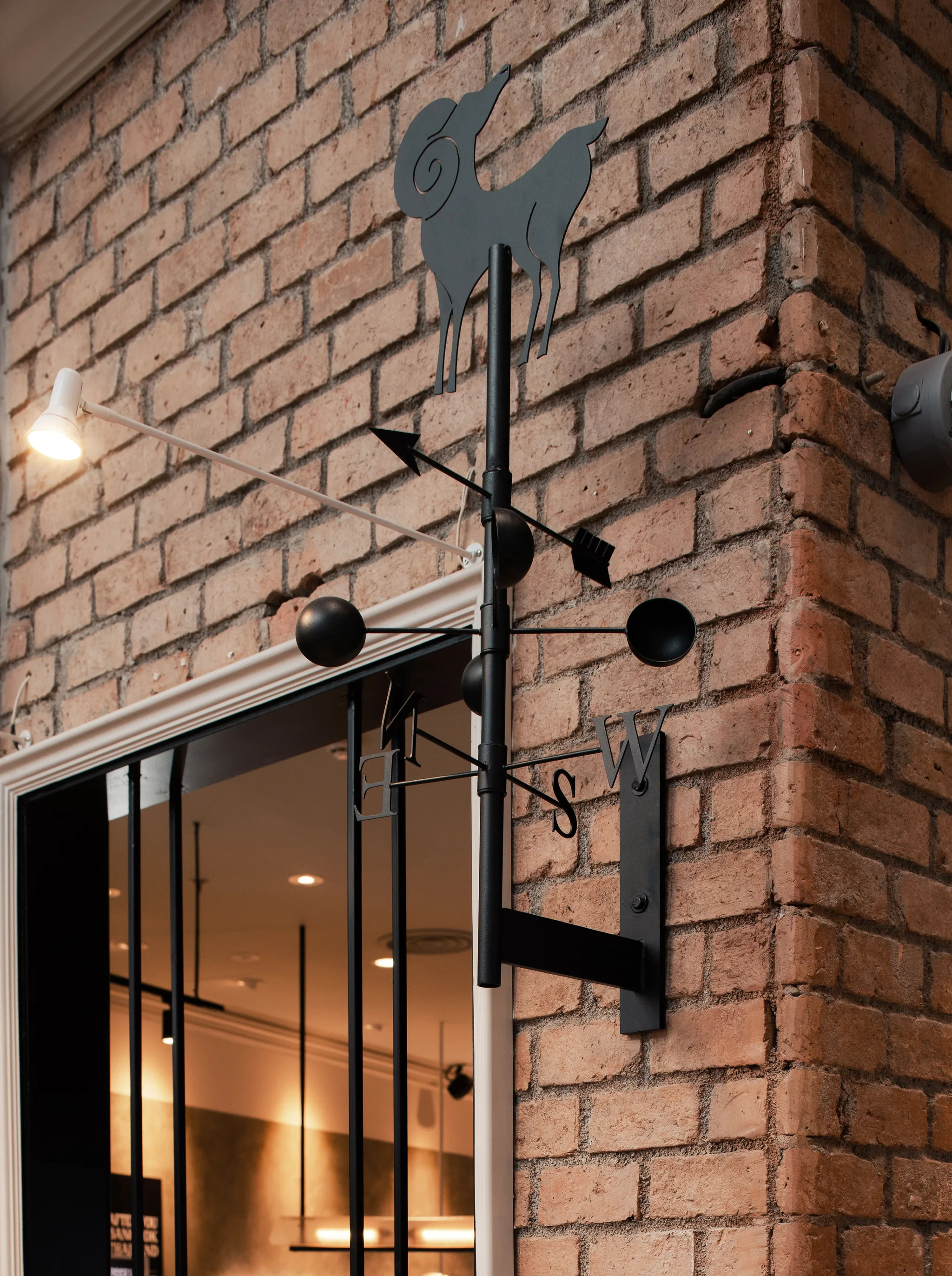 Black metal rooster sign and wall light fixed to a brick facade pier.