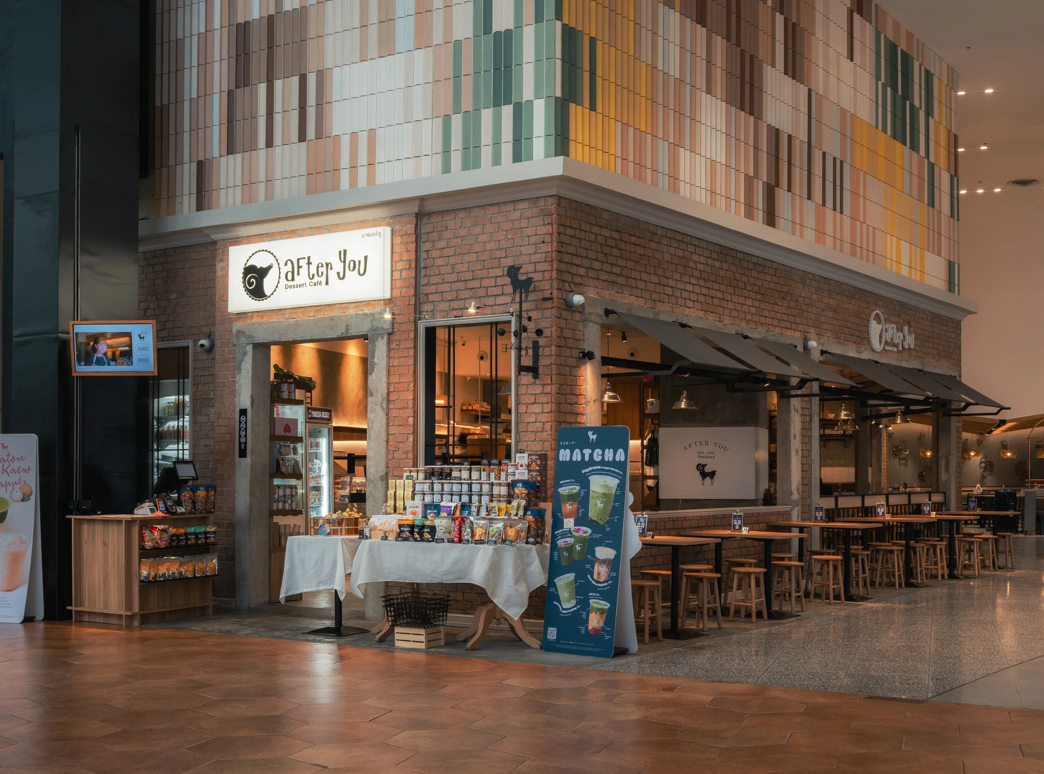 Corner arrival showing the open brick facade, product display and cafe seating.