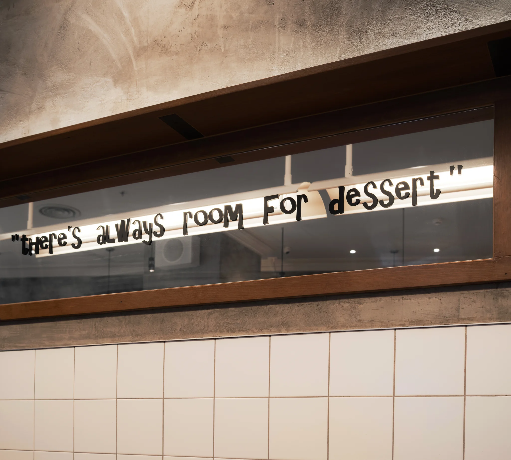 Handwritten dessert quote reflected above white tile and timber seating.
