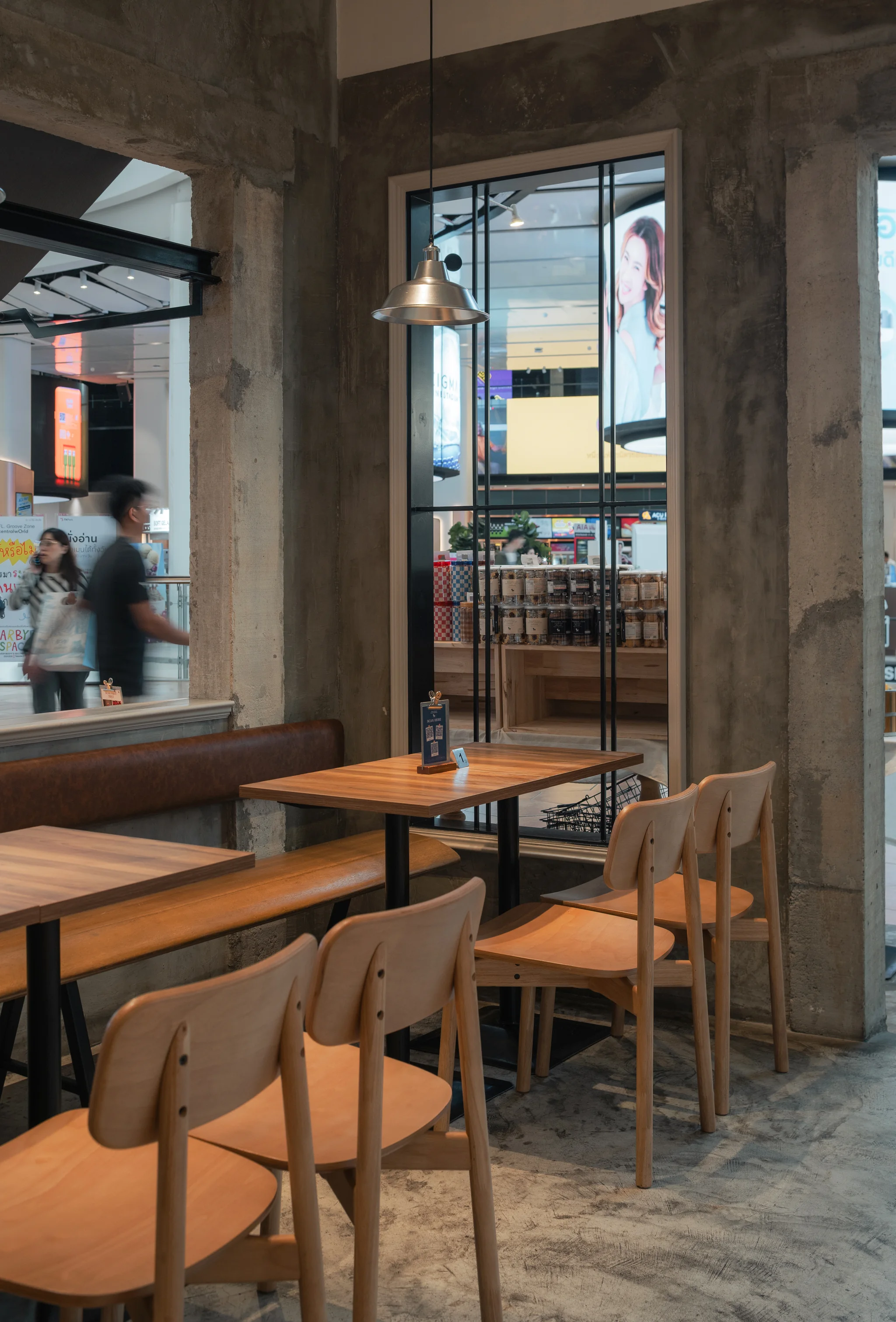 Timber chairs and tables positioned along a concrete-framed shopfront opening.