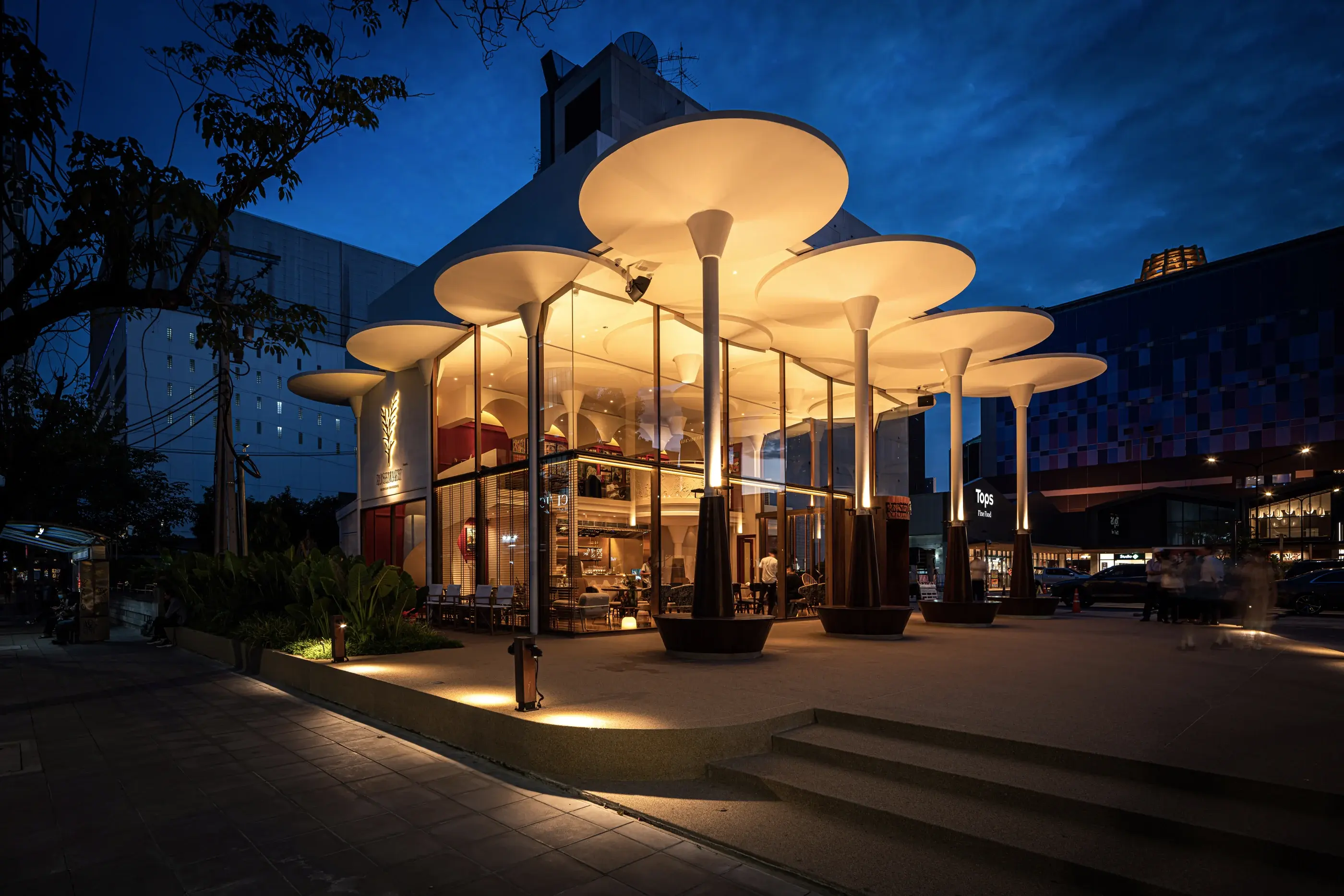 Rosemary Everyday Brasserie illuminated at blue hour beneath sculptural circular canopies
