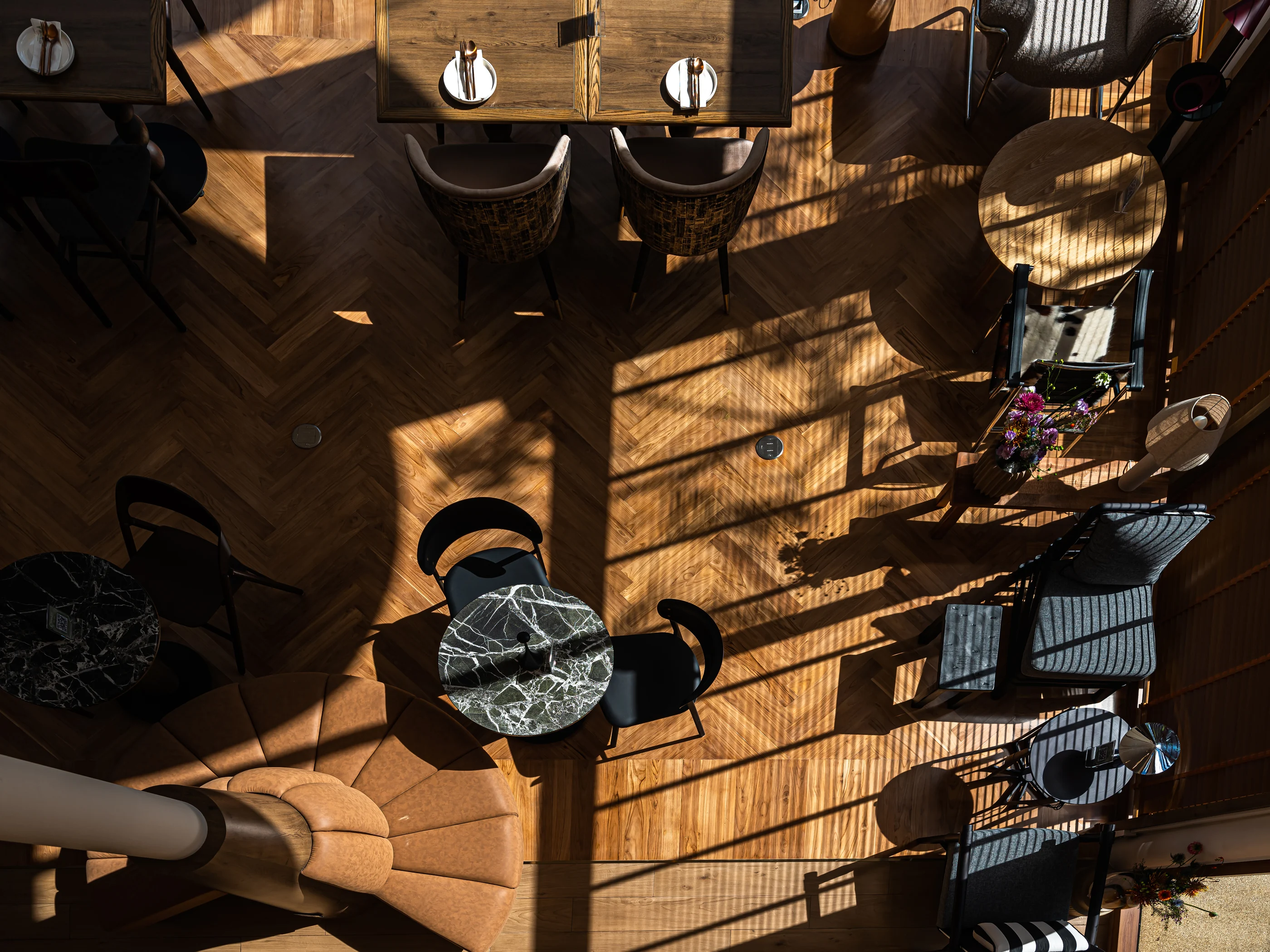 Overhead view of dining tables, herringbone timber floor and patterned sunlight