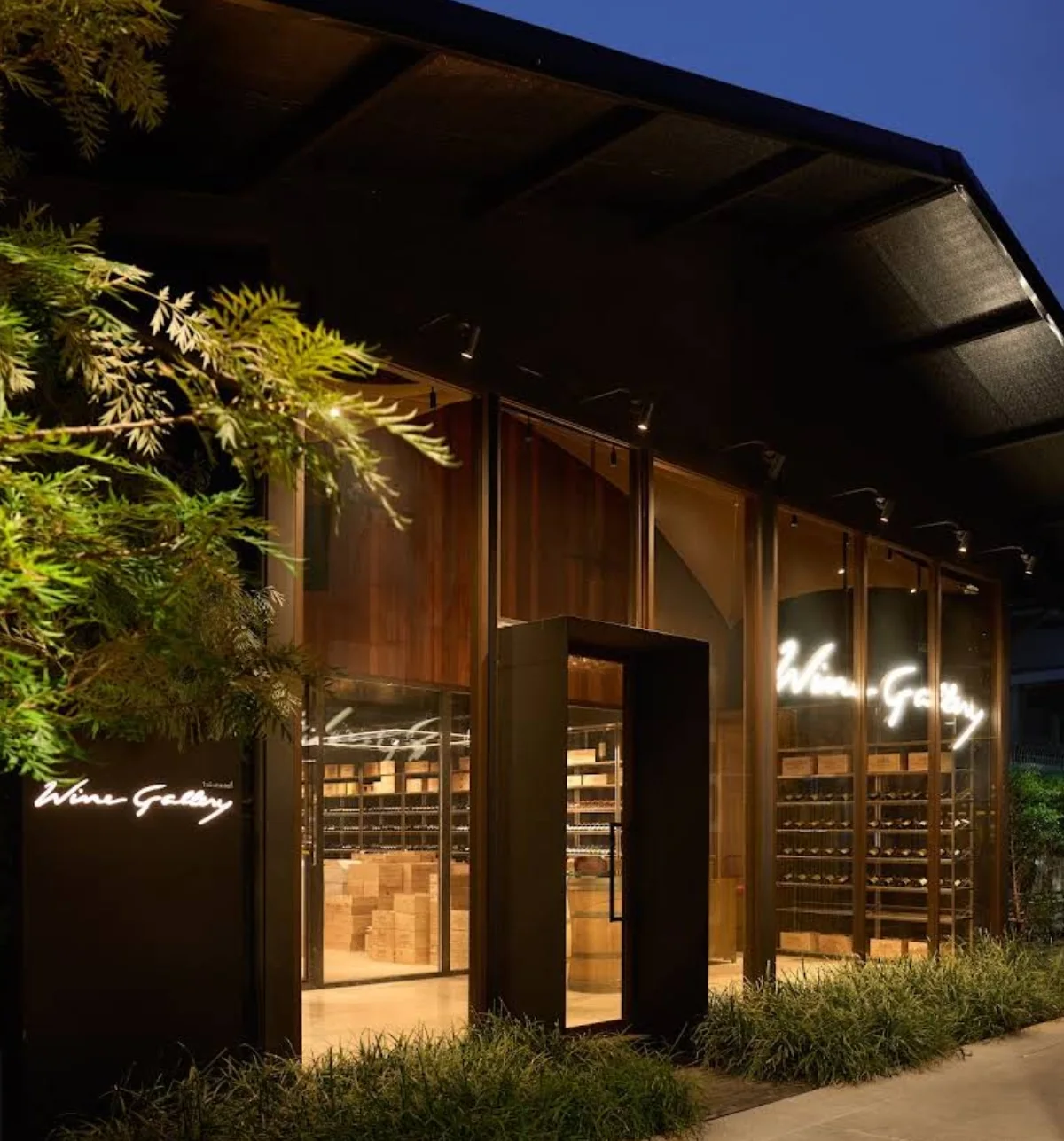Night exterior of Wine Gallery Bangkok with black facade, full-height glazing and illuminated interior